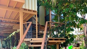 Una escalera con escalones de madera y barandillas metálicas, rodeada de abundante follaje y plantas en macetas.