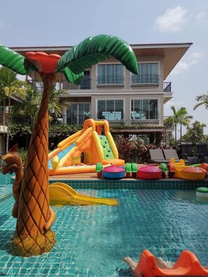 Une piscine avec des toboggans et des jeux gonflables, entourée de palmiers et bordée d’un bâtiment doté de balcons.