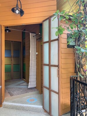 Une entrée en bois avec une porte coulissante en verre, un petit espace de porche et un pot de fleurs.