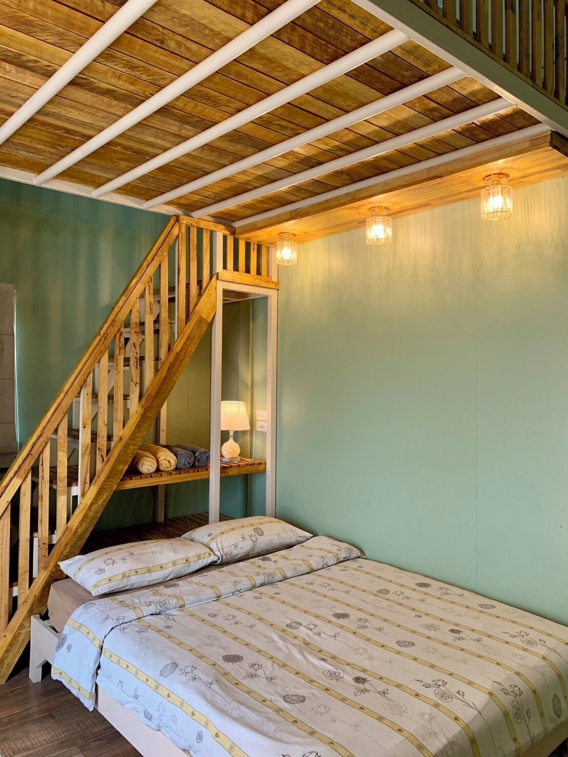 Een slaapkamer met een houten trap, een bed met bloemenbeddengoed en een nachtkastje met een lamp.
