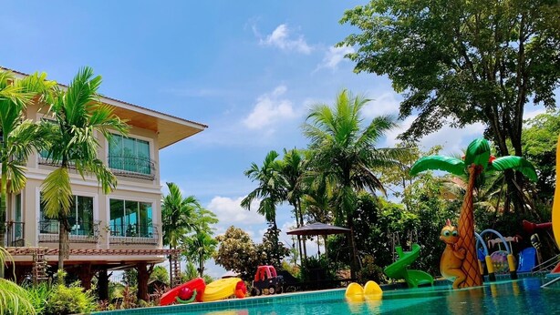 Una piscina con juguetes inflables, palmeras y un edificio con amplias ventanas.