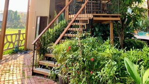 Una escalera exterior de varios niveles rodeada de abundante vegetación, que conduce a un balcón con barandilla.