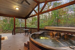 Una terraza de madera con un jacuzzi, una mesa y sillas, con vistas a un área boscosa.
