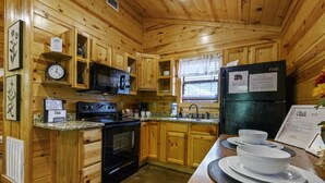 A wooden cabin kitchen with a stove, microwave, refrigerator, and wooden cabinets. - Cozy cabin-Great Location (Hochatown)