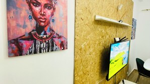 A room with a wooden wall panel, a mounted TV, a white cabinet, and a painting. - Aconchegante Apartamento na Marginal de Luanda, Para uma Estadia Confortável (Luanda)