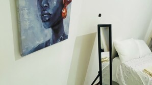 A bedroom with a bed, a bedside table, and a wall-mounted painting. - Aconchegante Apartamento na Marginal de Luanda, Para uma Estadia Confortável (Luanda)