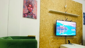 A living room with a green sofa, a white ottoman, a mounted TV, and a wooden wall panel. - Aconchegante Apartamento na Marginal de Luanda, Para uma Estadia Confortável (Luanda)