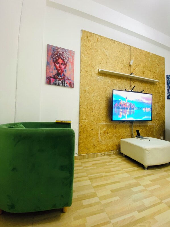 A living room with a green sofa, a white ottoman, a mounted TV, and a wooden wall panel.