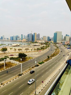 A cityscape with modern buildings, a curved road, and a waterfront area with palm trees.