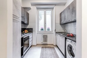 Eine kompakte Küche mit Einbauofen, Waschmaschine und einem Fenster mit Blick auf Grünflächen.