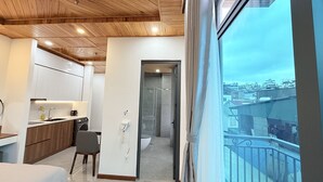 A modern hotel room with a wooden ceiling, a balcony with a city view, a kitchenette, and a separate bathroom. - Hasa Da Lat Hotel and Apartment (Xuan Huong - Da Lat)