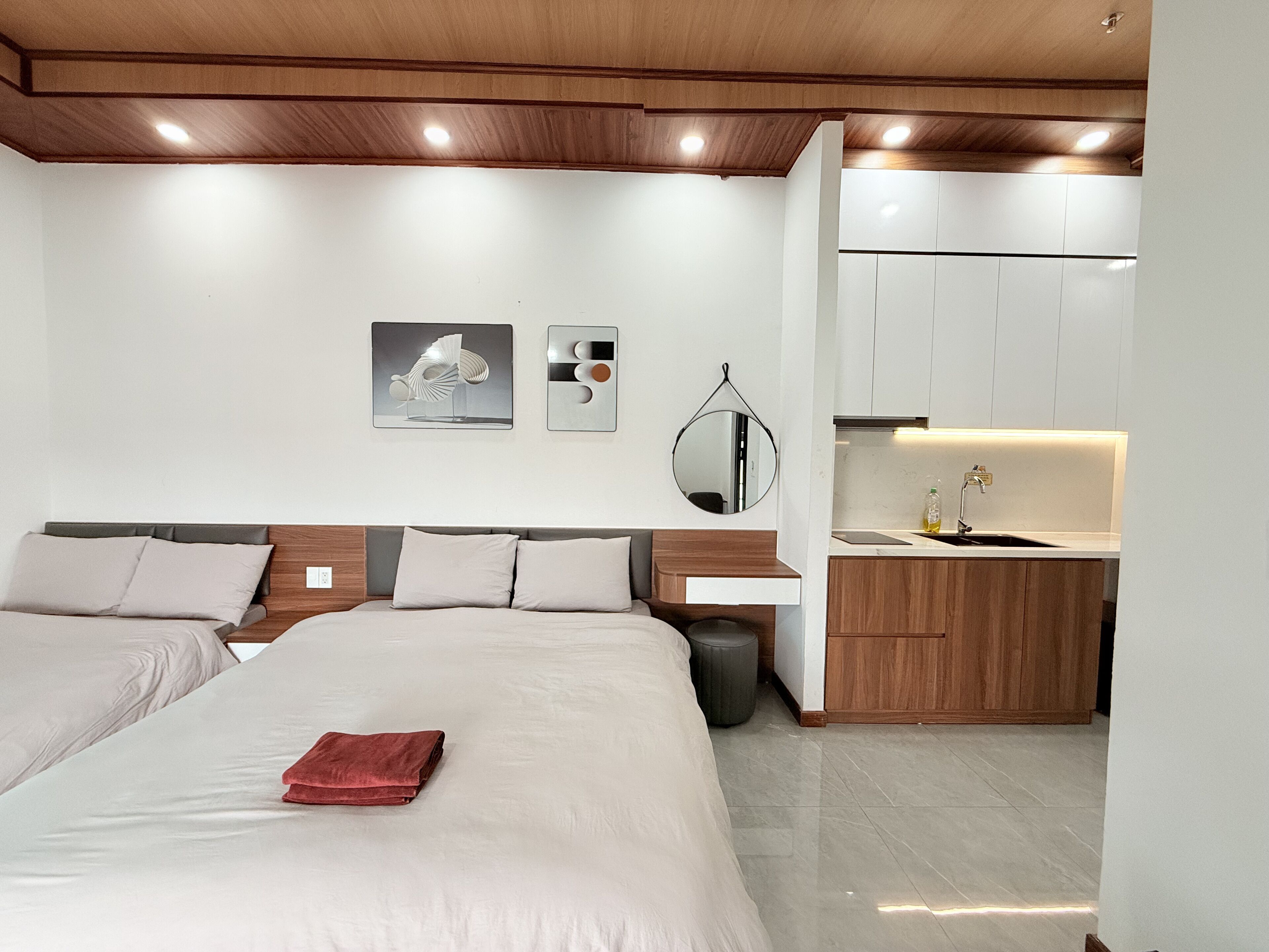 A modern hotel room with a large bed, a small kitchenette, and a wooden ceiling.
