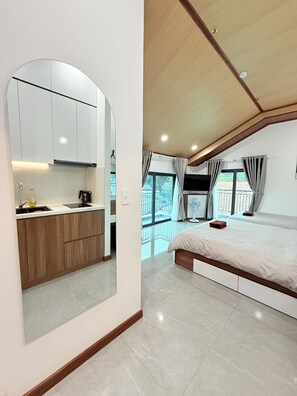 Ein modernes Schlafzimmer mit einem großen Bett, einem eingebauten Schreibtisch und einer Küchenzeile mit weißen Schränken und einer Holz Arbeitsplatte.