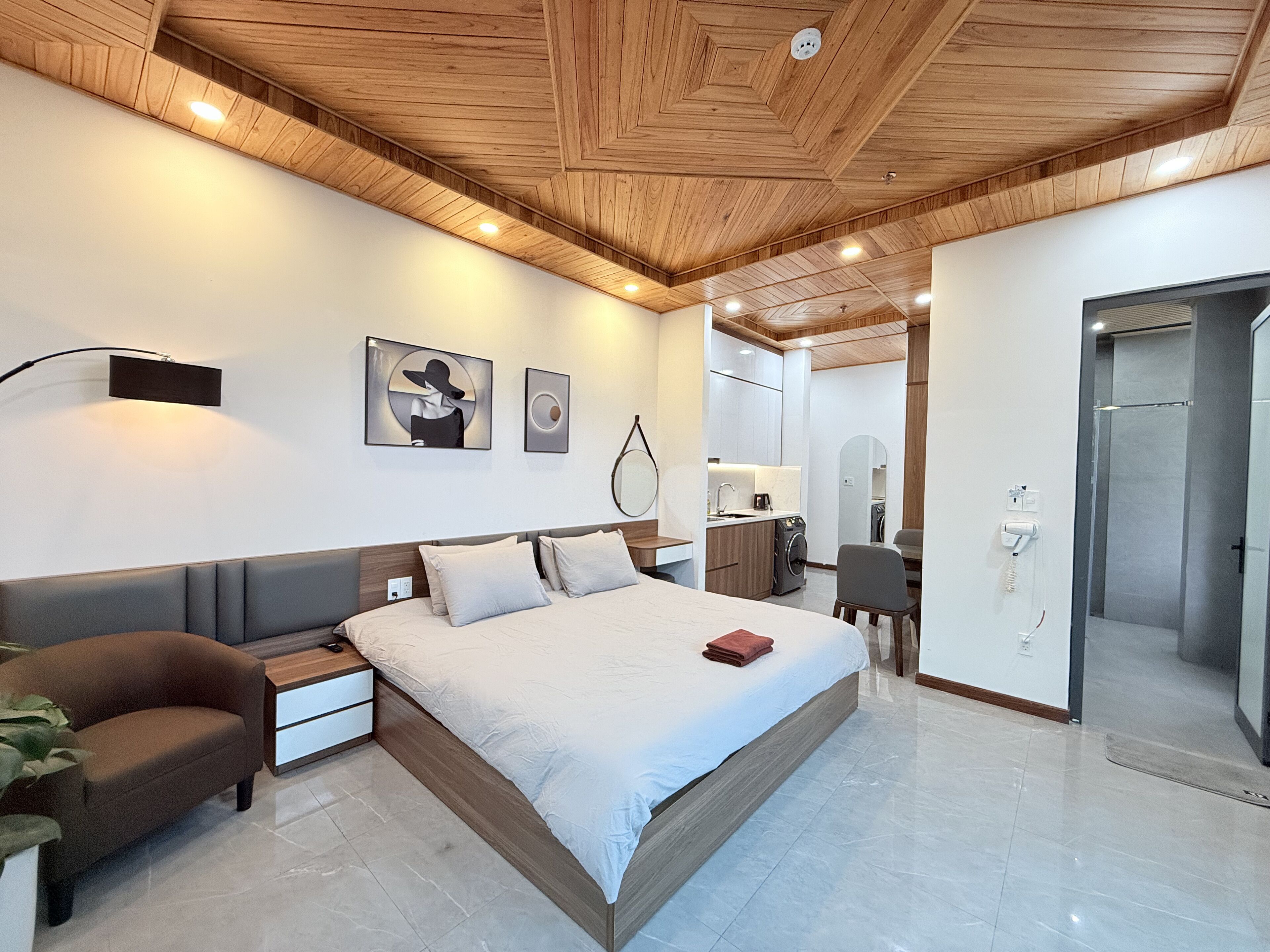 A modern bedroom with a wooden ceiling, a large bed, bedside tables, a desk, and a wardrobe.