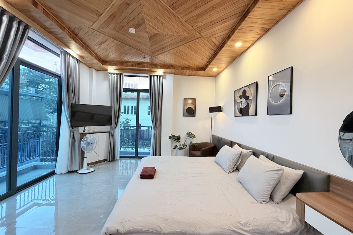 A modern bedroom with a large bed, a TV, and a balcony with curtains.