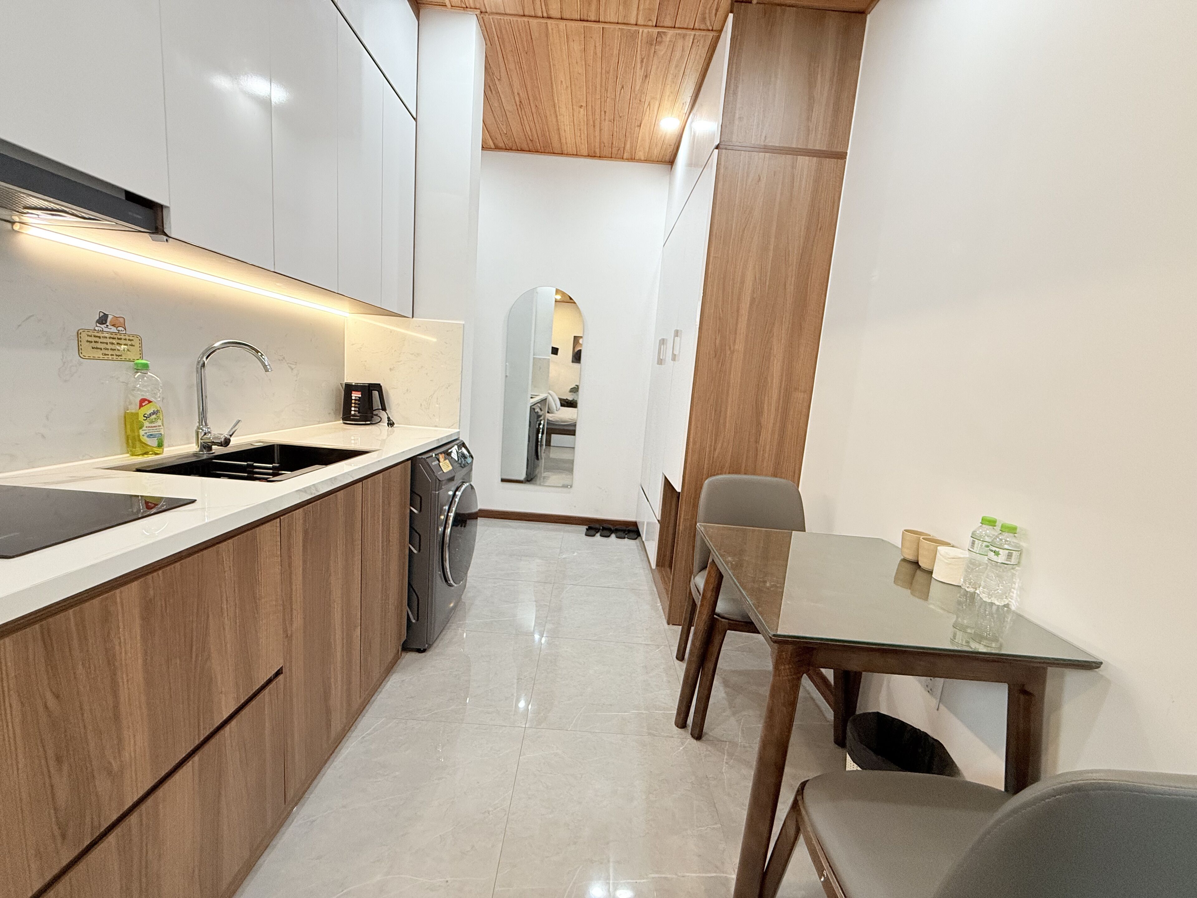 Une cuisine compacte dotée d’un lave-linge intégré, un coin repas avec une table et des chaises, et une vue sur l’espace de vie adjacent.