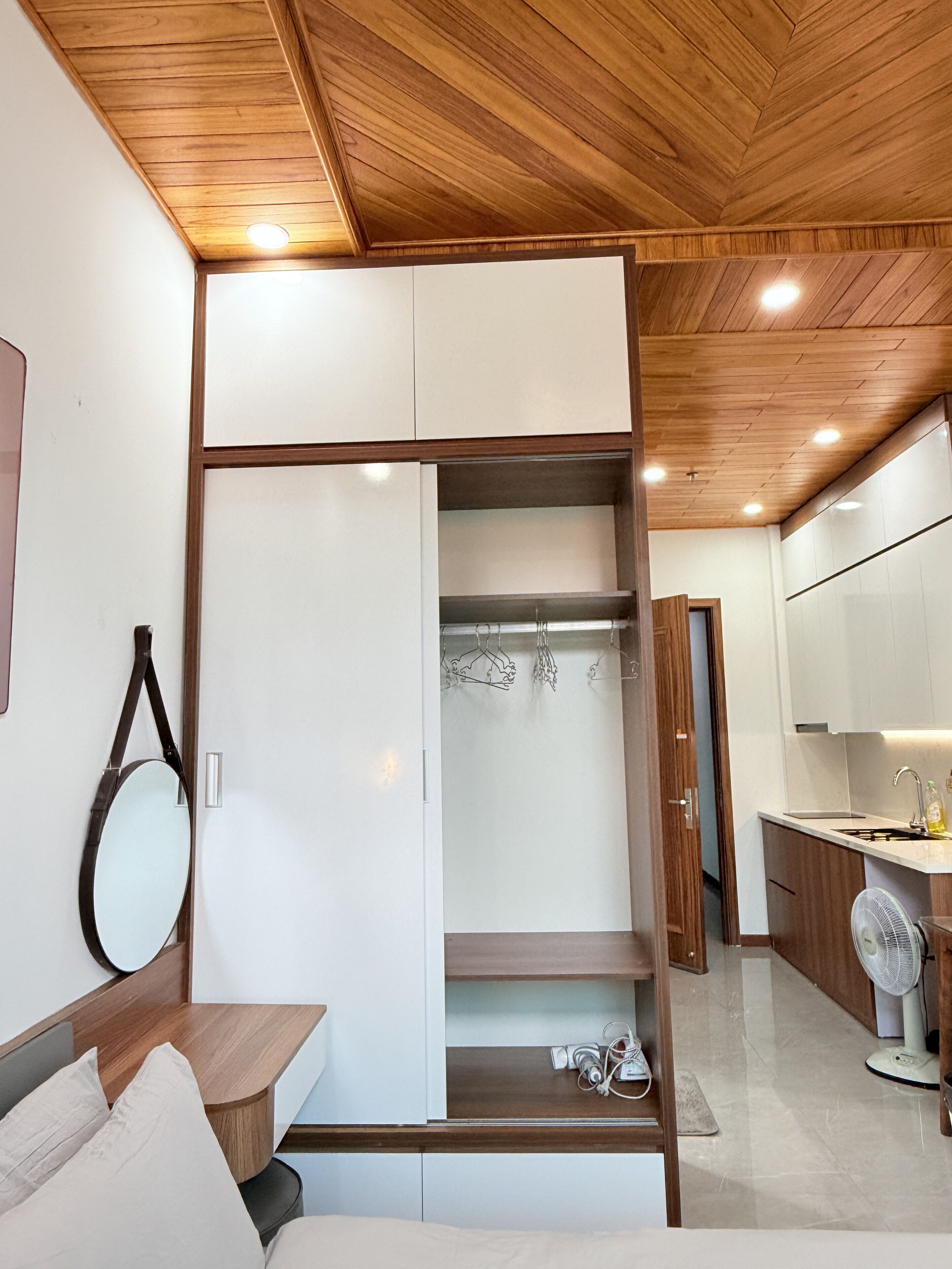 Une chambre moderne avec un plafond en bois, une armoire intégrée avec espace pour suspendre les vêtements, une table de chevet et un grand miroir.