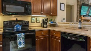 A kitchen with wooden cabinets, a black microwave, a stove, and a dishwasher.