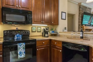 A kitchen with wooden cabinets, a black microwave, a stove, and a dishwasher. - Scenic 2BR Condo w/ Porch + Pool Near Slope/Trails | Free Tickets (Maggie Valley)
