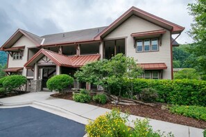 A two-story house with a covered porch, a stone foundation, and a landscaped front yard with various shrubs and flowers.