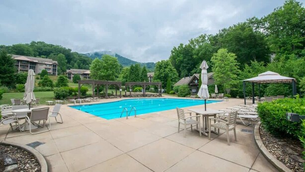 A swimming pool with lounge chairs and umbrellas, surrounded by greenery and buildings.