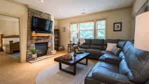 A living room with a stone fireplace, a leather sofa, and a flat-screen TV.