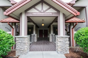 The entrance to 1560 Country Club Dr. with a covered walkway, stone pillars, and a sign above the doors. - Scenic 2BR Condo w/ Porch + Pool Near Slope/Trails | Free Tickets (Maggie Valley)