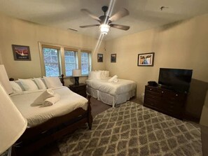A bedroom with two beds, a ceiling fan, a TV, and framed pictures on the walls.