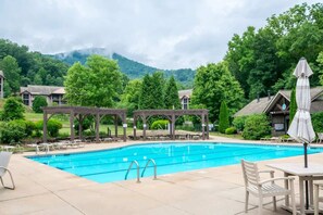 Ein Schwimmbecken mit Liegestühlen und Sonnenschirmen, umgeben von Bäumen und Gebäuden.