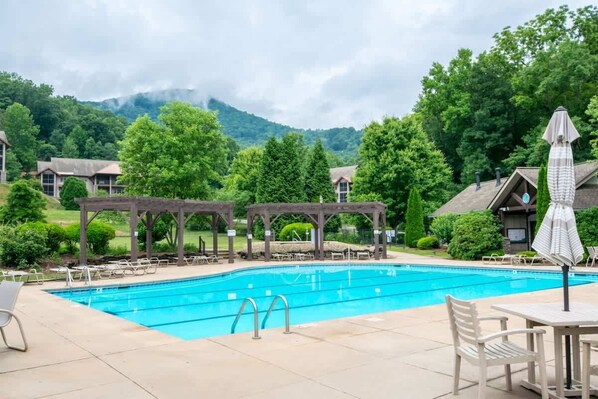 A swimming pool with lounge chairs and umbrellas, surrounded by trees and buildings.