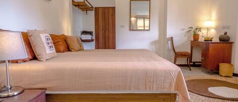 Un dormitorio con cama, mesita de noche, lámpara, cómoda, espejo y una pequeña alfombra.