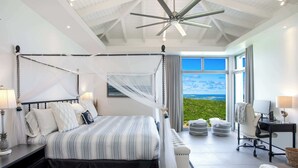 A four-poster bed with a canopy, a desk with a chair, and a view of the landscape through large windows. - Five Minutes More (4 bedrooms) - Luxury villa with pool, Oyster Pond, St. Maarten (Oyster Pond)