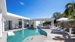 A modern pool area with a clear pool, wooden deck, lounge chairs, and a stone wall. - Five Minutes More (4 bedrooms) - Luxury villa with pool, Oyster Pond, St. Maarten (Oyster Pond)