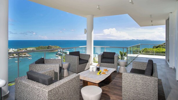 A balcony with wicker furniture, a table with food, and a view of the sea and coastline. - Five Minutes More (4 bedrooms) - Luxury villa with pool, Oyster Pond, St. Maarten (Oyster Pond)