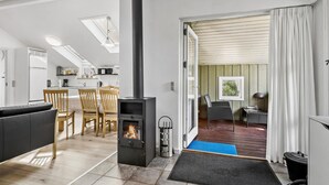 A modern kitchen with a skylight, a dining area with wooden chairs, a black sofa, and a fireplace.