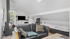 A modern, compact living space with a loft bed, a flat-screen TV, a sofa, and a dining area.