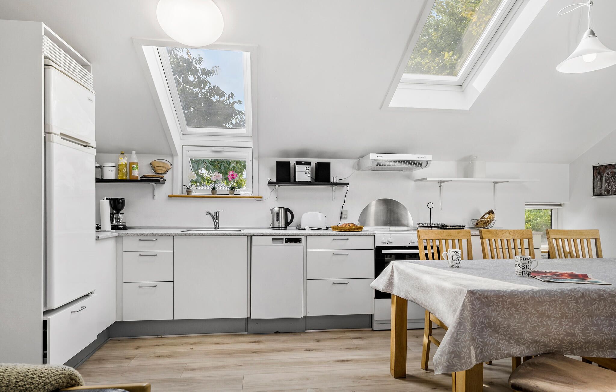 Una cocina moderna con armarios blancos, un comedor con mesa y un tragaluz.