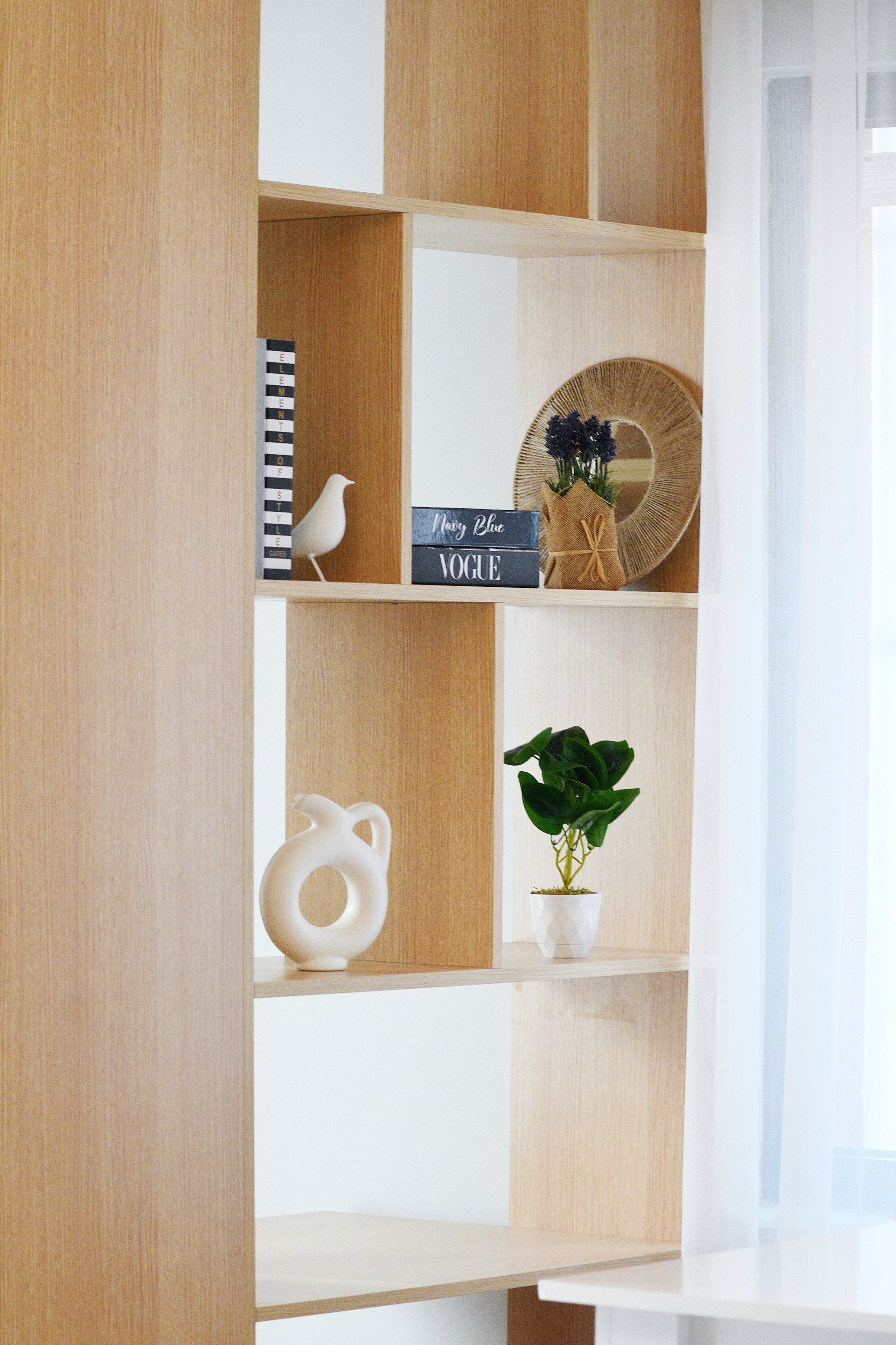 Ein Holzregal mit Büchern, einer Vogelstatue, einem Zier-Spiegel und einem Topfpflanzen.