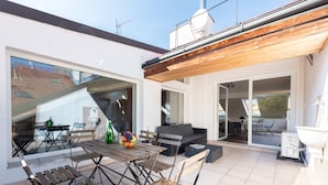 Une terrasse extérieure moderne, dotée d’une table et de chaises en bois, d’un canapé et d’un barbecue.