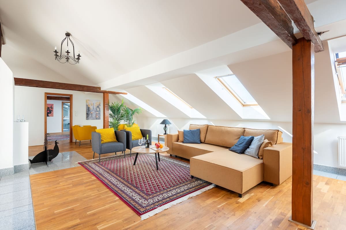 A spacious loft with a high ceiling, skylights, a modern sofa, a coffee table, and a patterned rug.