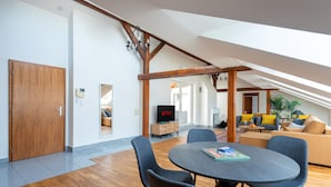 Un vaste espace de vie doté d’un plafond haut, de poutres en bois, d’une table ronde avec des chaises, d’un canapé et d’un téléviseur.