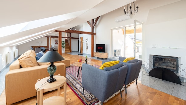 Un salon moderne avec un canapé, un fauteuil et une cheminée. On y trouve également une télévision et une lampe sur une table.