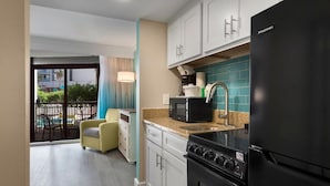 A modern kitchen with a black refrigerator, a microwave, and a stove. There is a window with a view of a pool and a chair outside. - Resort View Two Room Condo Family-Friendly (Myrtle Beach)