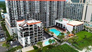 A multi-story hotel with a rooftop pool, outdoor seating, and a well-maintained lawn. - Resort View Two Room Condo Family-Friendly (Myrtle Beach)