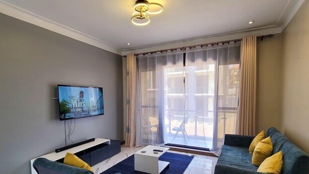A modern living room with a flat-screen TV, two sofas, a coffee table, and a large window with curtains. - Starlight Homes (Kampala)