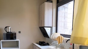 A compact kitchen with a microwave, stove, and sink. There is a small shelf and a trash bin. - Starlight Homes (Kampala)