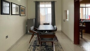 A dining area with a table and chairs, a rug, a TV, and a window with curtains. - Starlight Homes (Kampala)