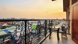 Un balcon doté d’une balustrade en fer forgé, d’une table et d’une chaise, offrant une vue sur un paysage urbain avec des bâtiments et un ciel dégagé.