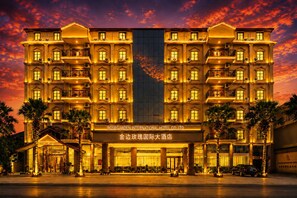 Een meerlaags hotel met een statig entree, grote zuilen en een goed verlichte gevel.