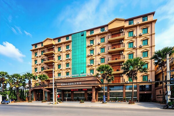 Un hotel de varios pisos con balcones, una franja verde vertical y palmeras al frente.